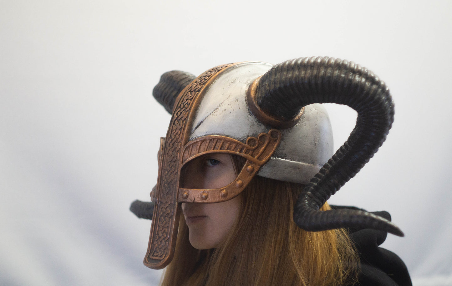 Person wearing a detailed helmet with horns on a plain background
