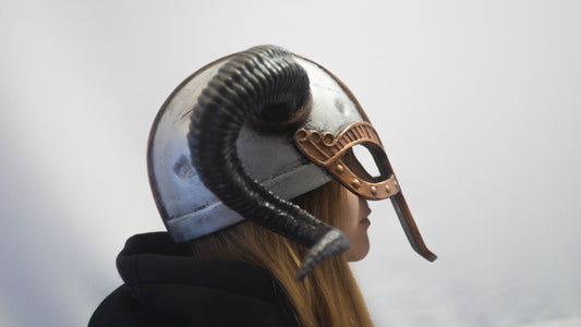 Person wearing a detailed helmet with ram's head design on a plain background