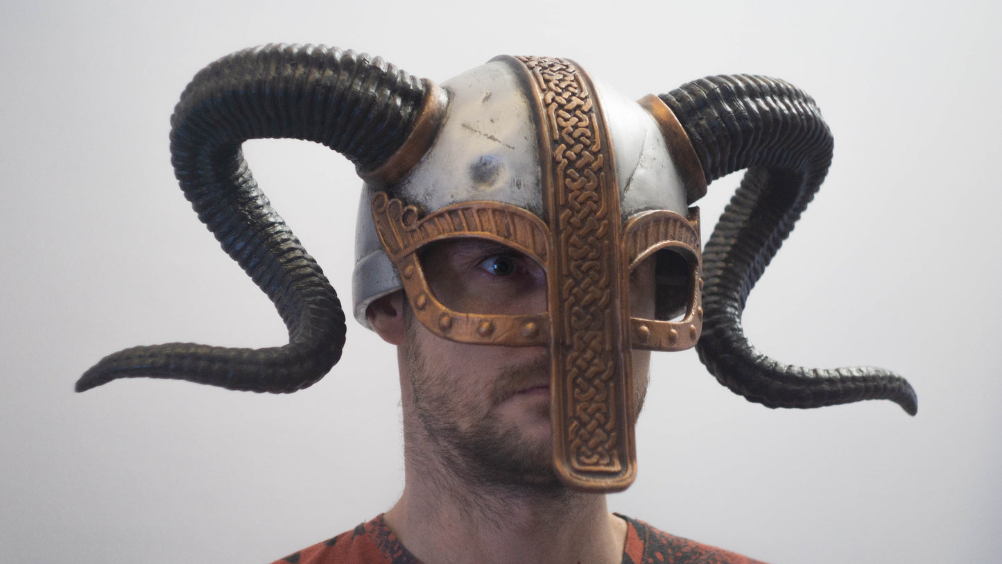 Person wearing a detailed helmet with ram horns on a plain background