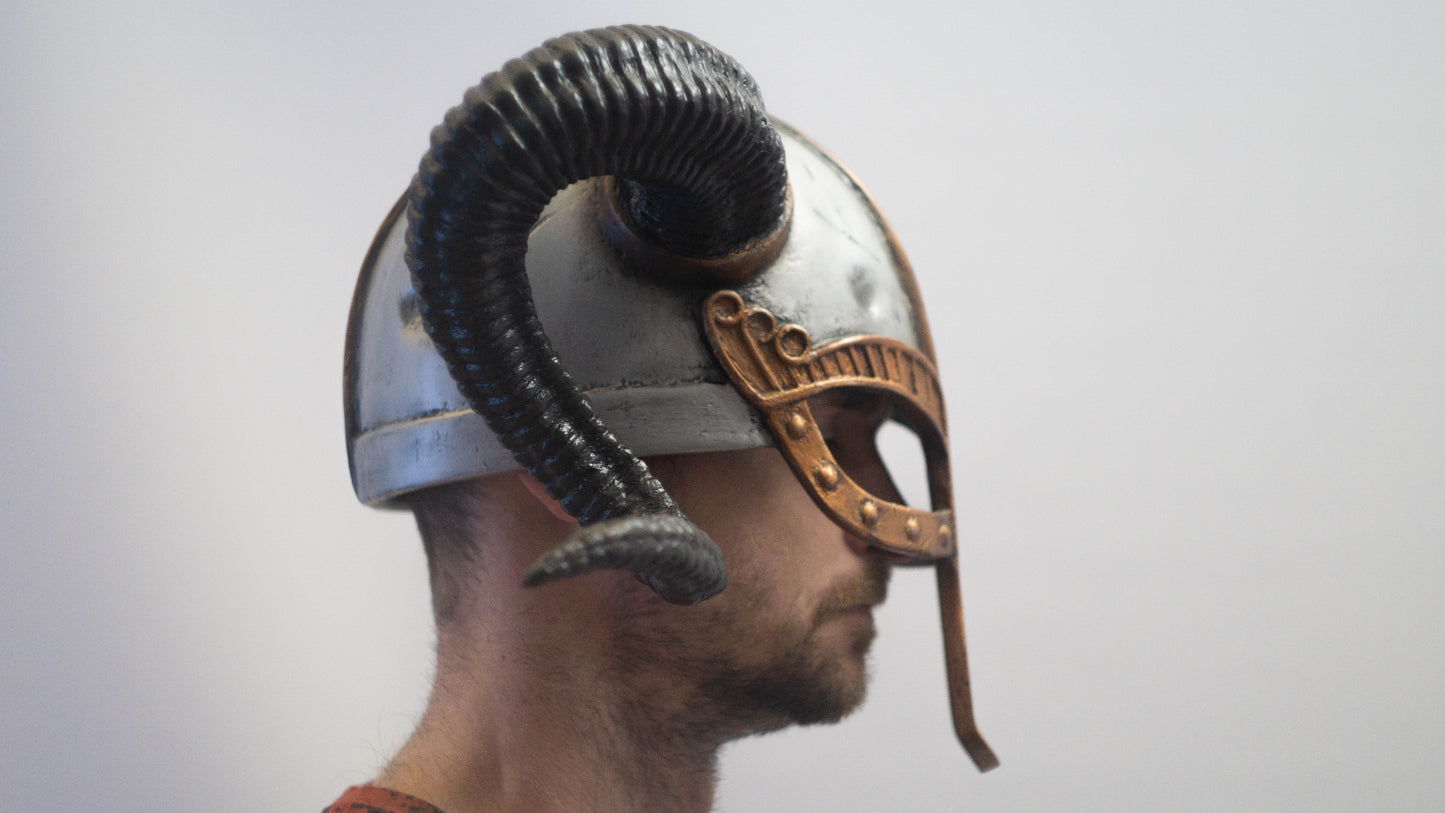 Person wearing a Roman-style helmet with a ram's head emblem on a plain background