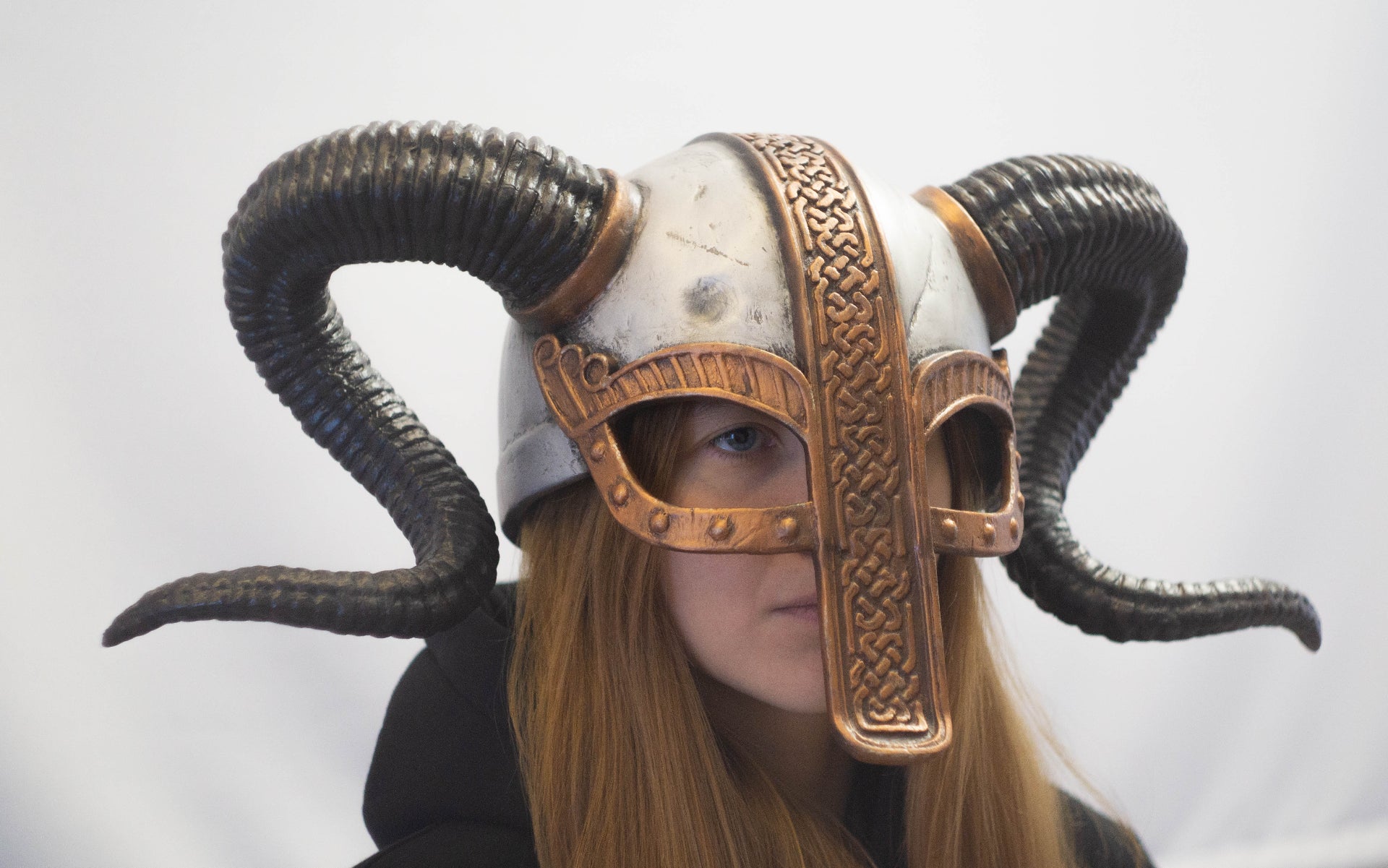 Person wearing a decorative helmet with ram horns on a plain background