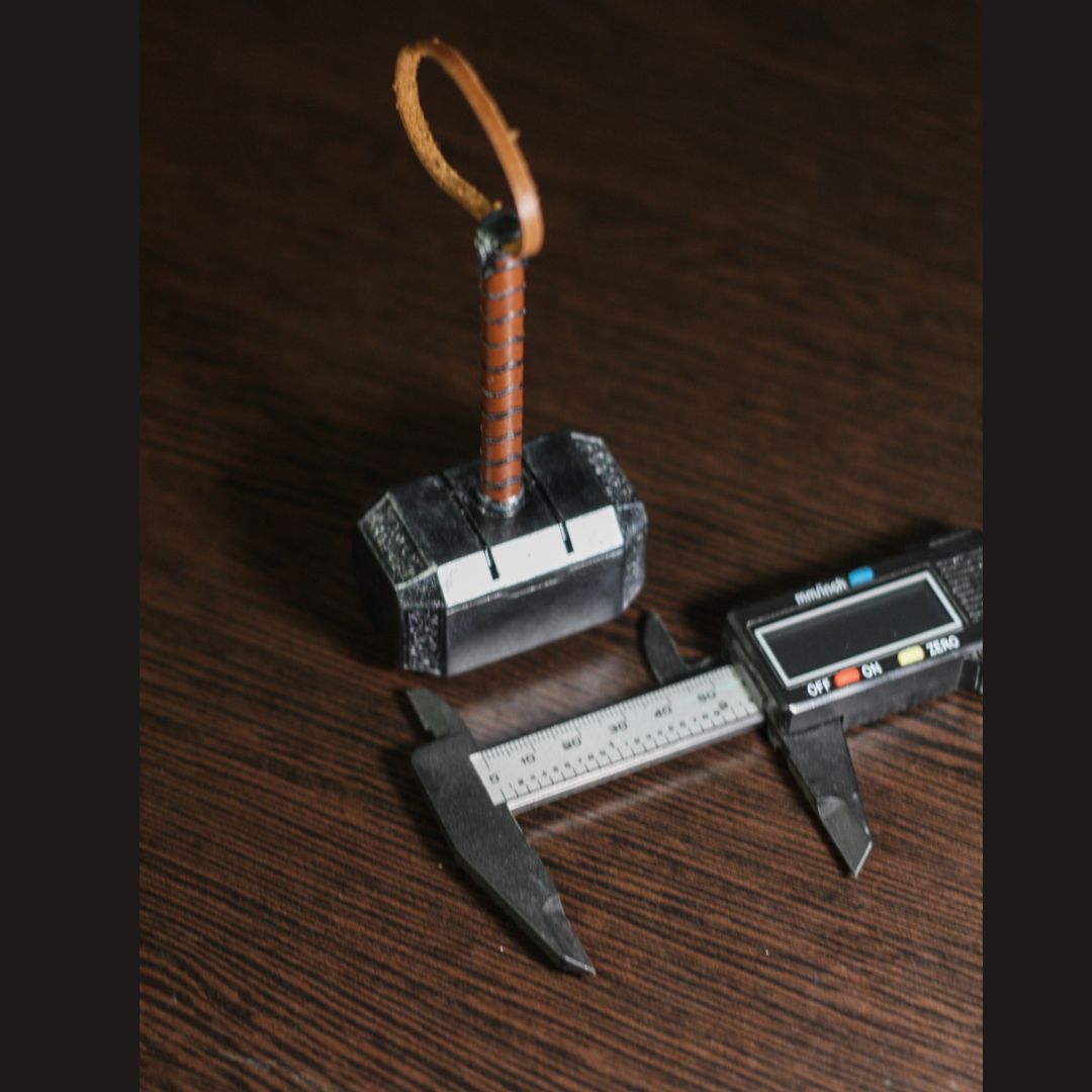 Thor Hammer miniature 1:4 scale replica with leather strap and caliper measuring its size on wooden surface