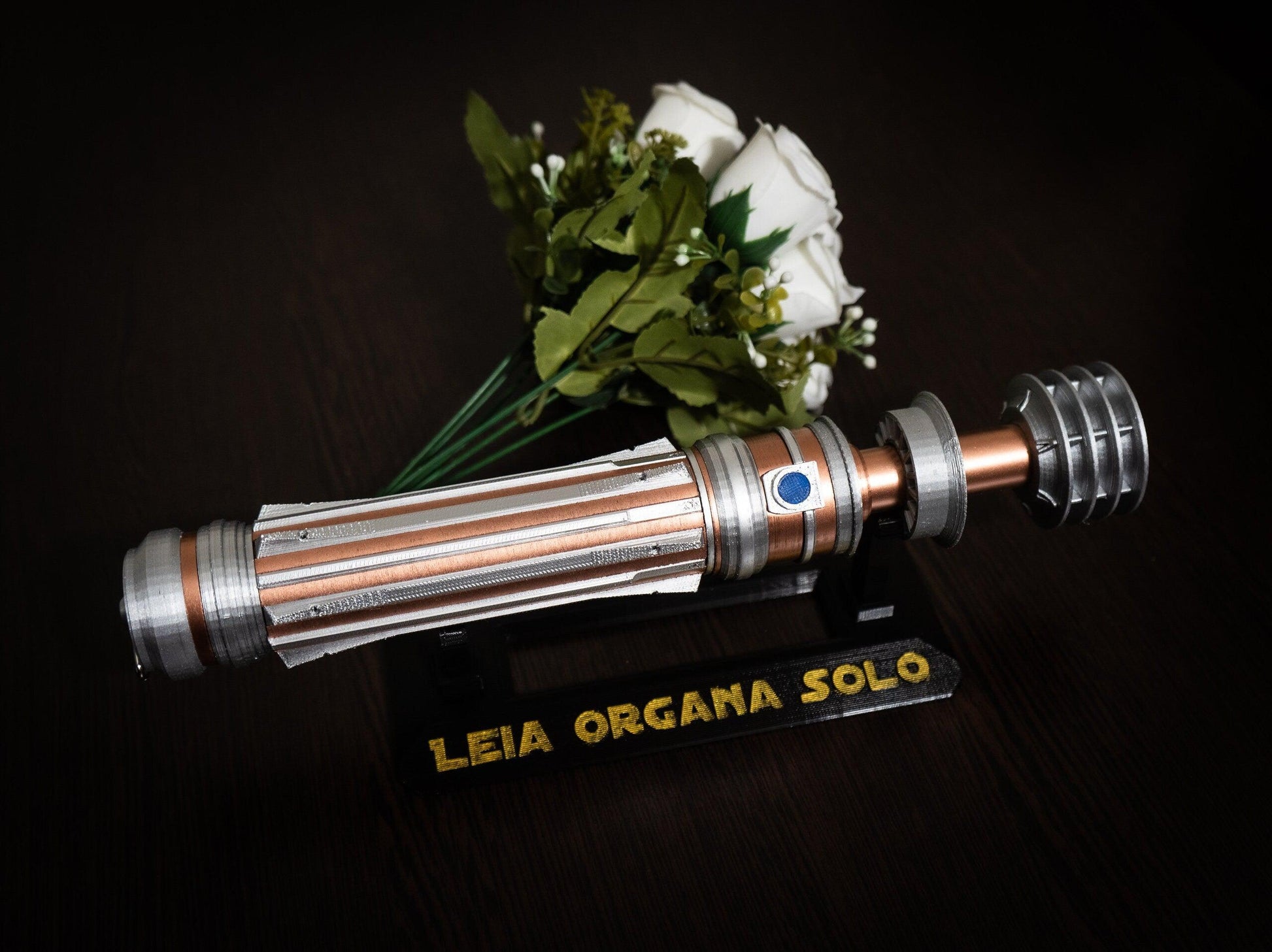 Star Wars inspired bridal bouquet holder shaped like Leia Organa's lightsaber hilt in copper and chrome colors with a wedding bouquet and display stand.