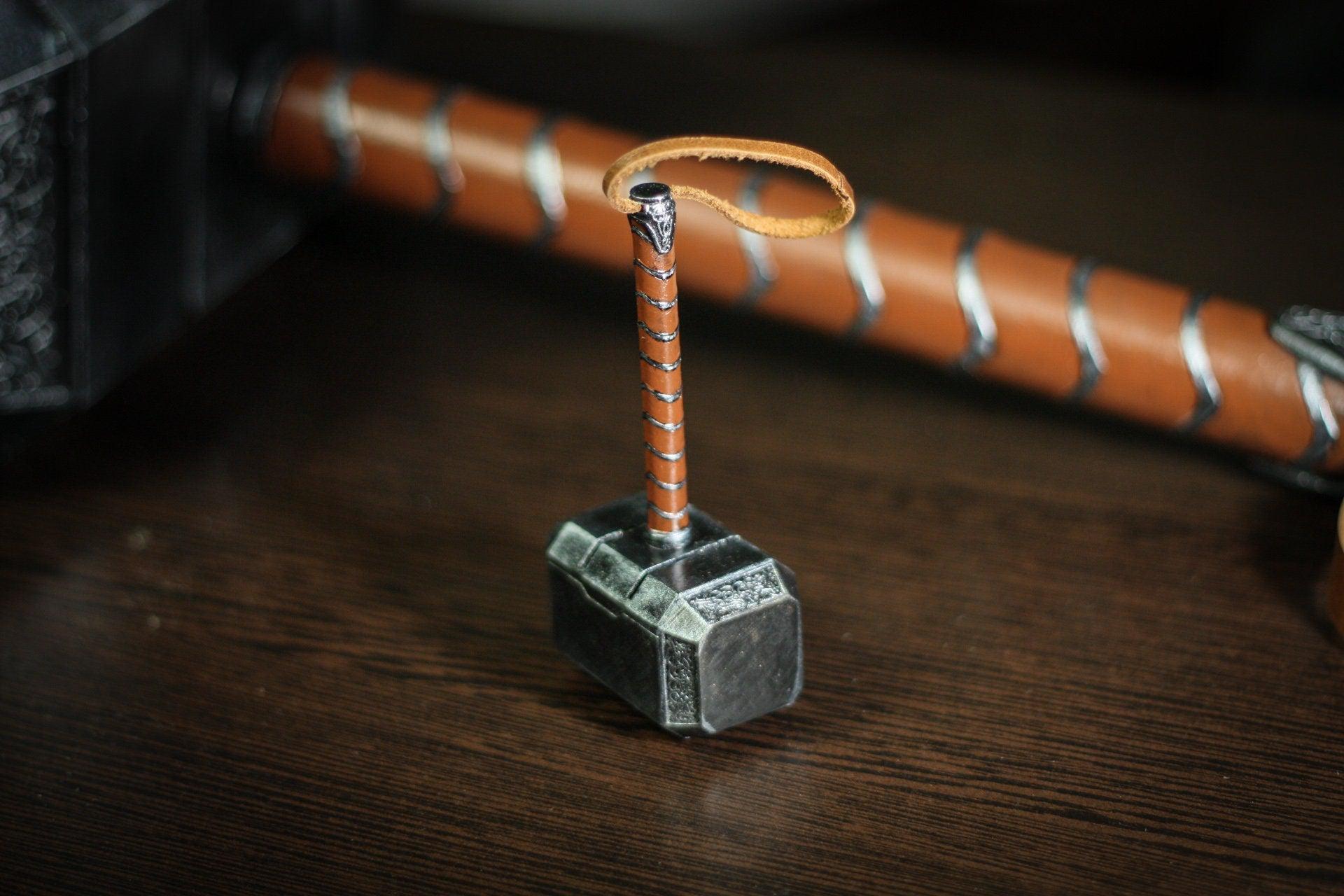 Thor hammer miniature 1:4 scale detailed resin replica with hand-painted finish and leather-wrapped handle on wooden surface.